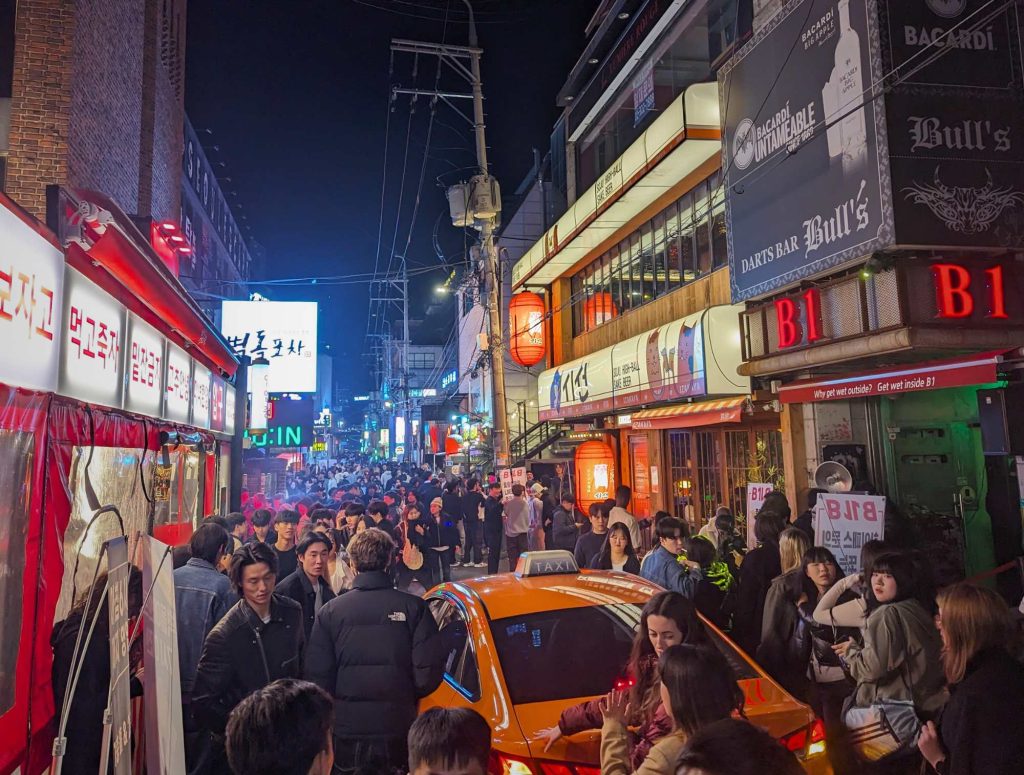 taxi moving through crowded party street in Hongdae